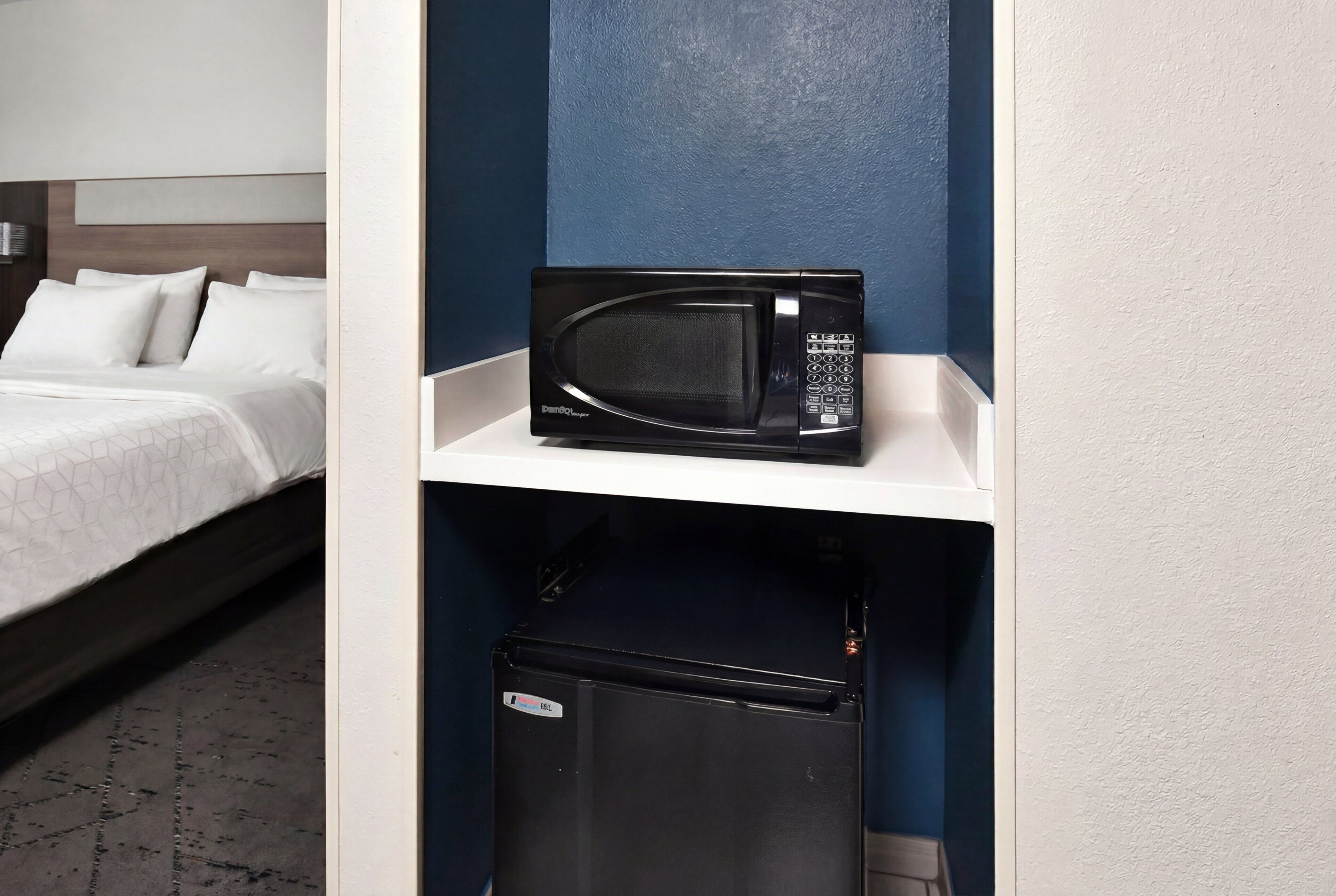 Een hotelkamer met een bed, een magnetron op een plank en een koelkast.