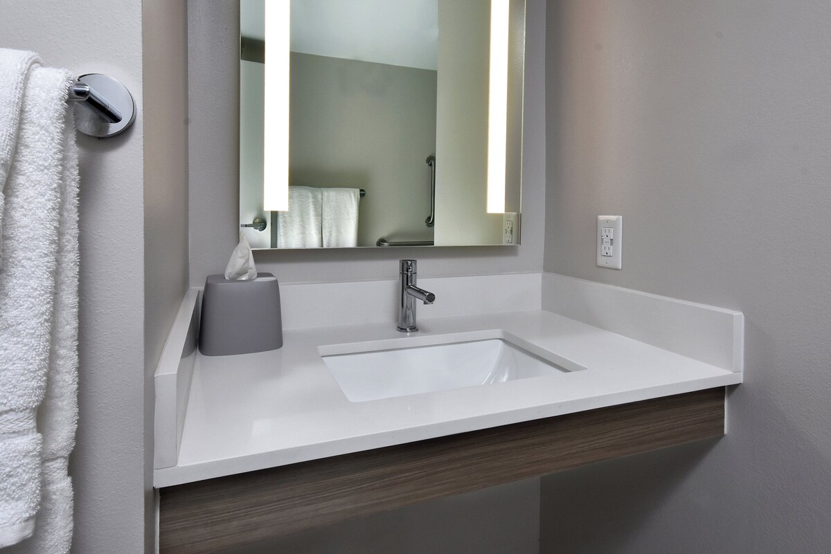 A bathroom with a white sink, a mirror, a towel dispenser, and a toilet paper holder.