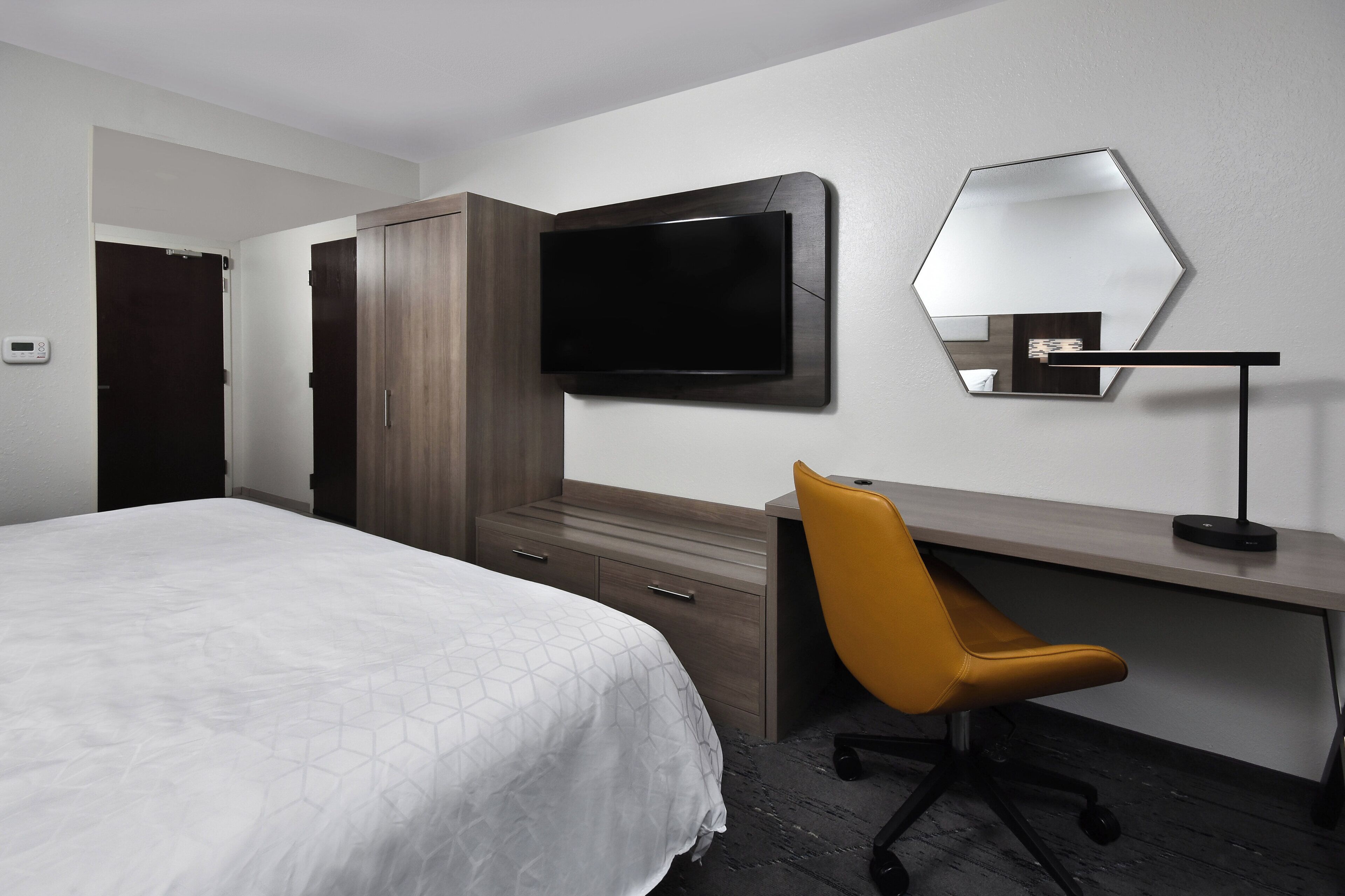 A hotel room with a bed, a desk, a chair, a television, and a mirror.