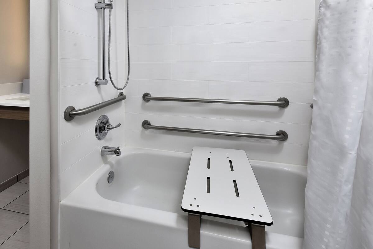 A modern bathroom with a white bathtub, grab bars, a showerhead, and a shower curtain.