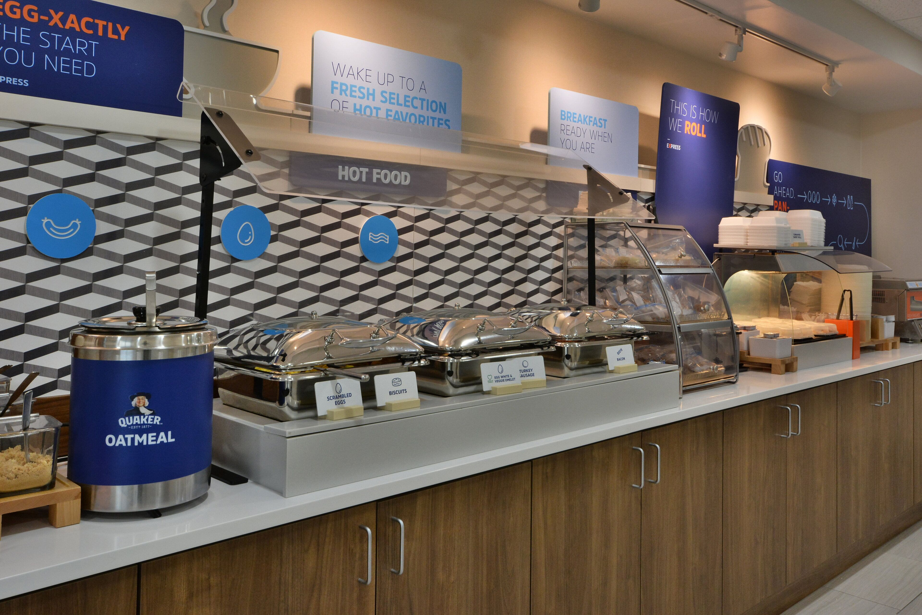 A breakfast buffet with labeled food containers, including oatmeal, scrambled eggs, and biscuits.