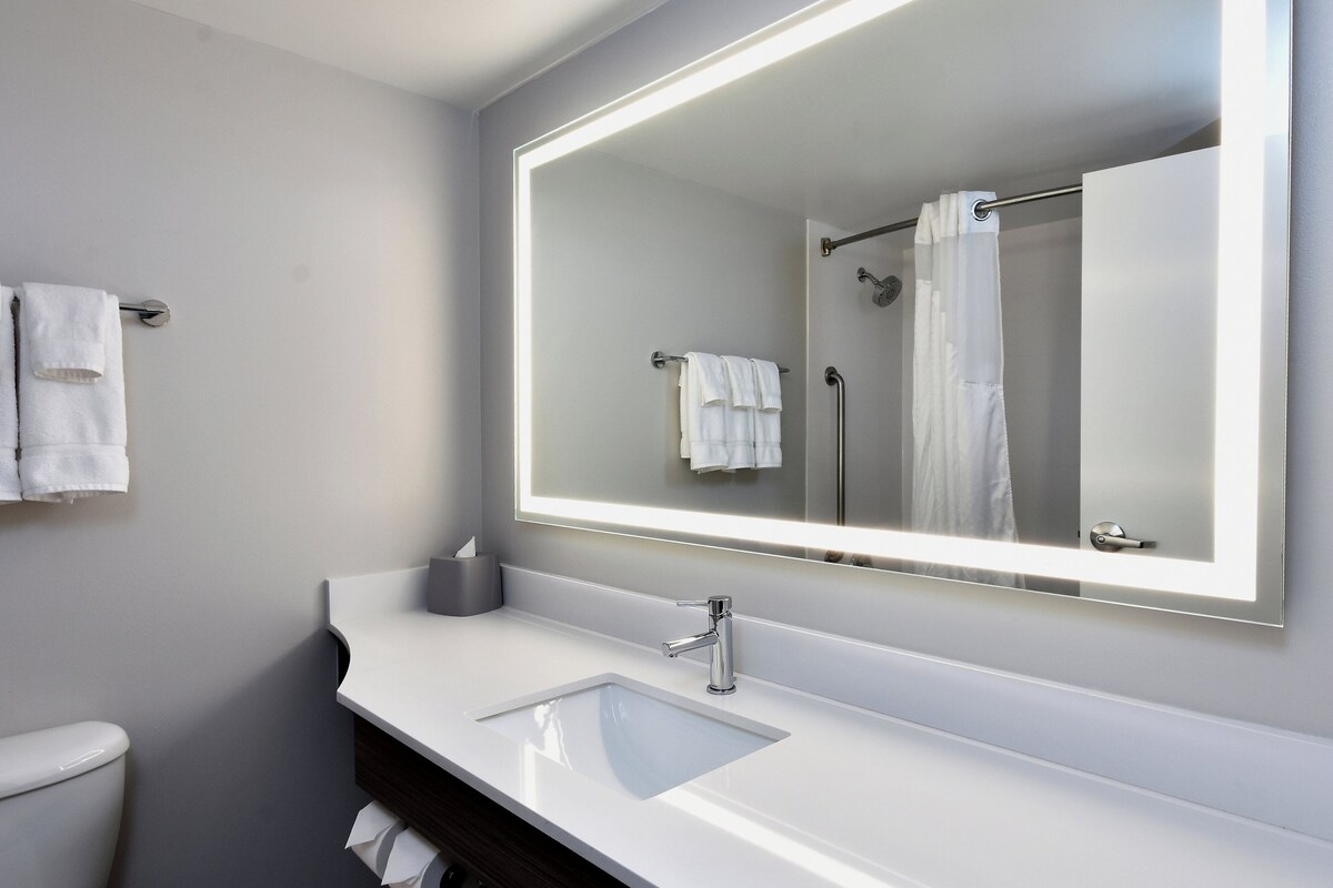 A modern bathroom with a large mirror, a white sink, and a shower area.