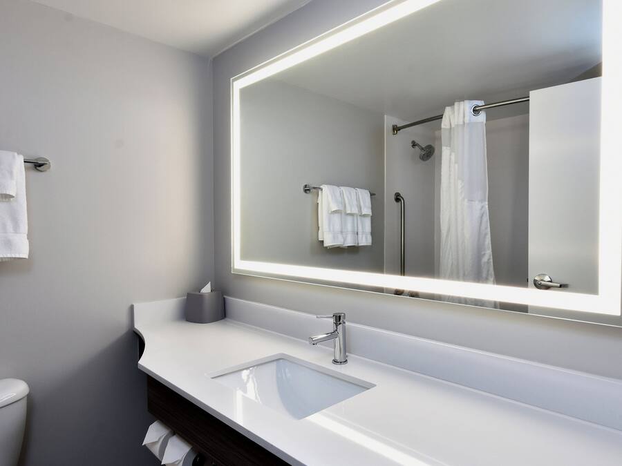 A modern bathroom with a large mirror, white sink, and a towel rack.