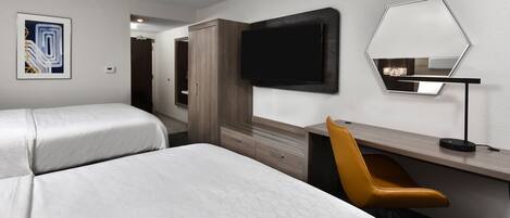 A hotel room with two beds, a desk, a chair, a TV, and a mirror.