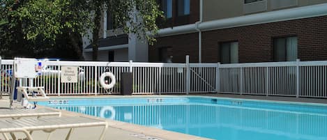 A swimming pool with a white fence, lounge chairs, and a lifebuoy.