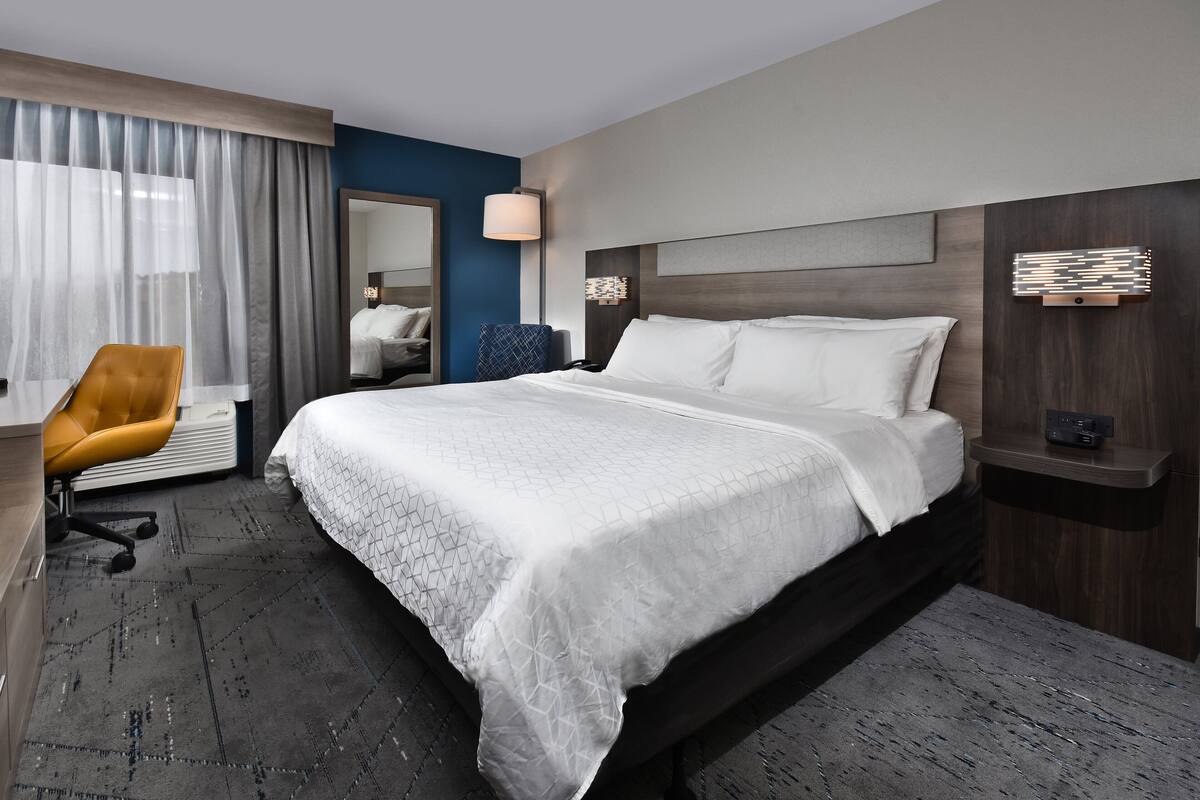 A hotel room with a large bed, a chair, a desk, and a mirror.