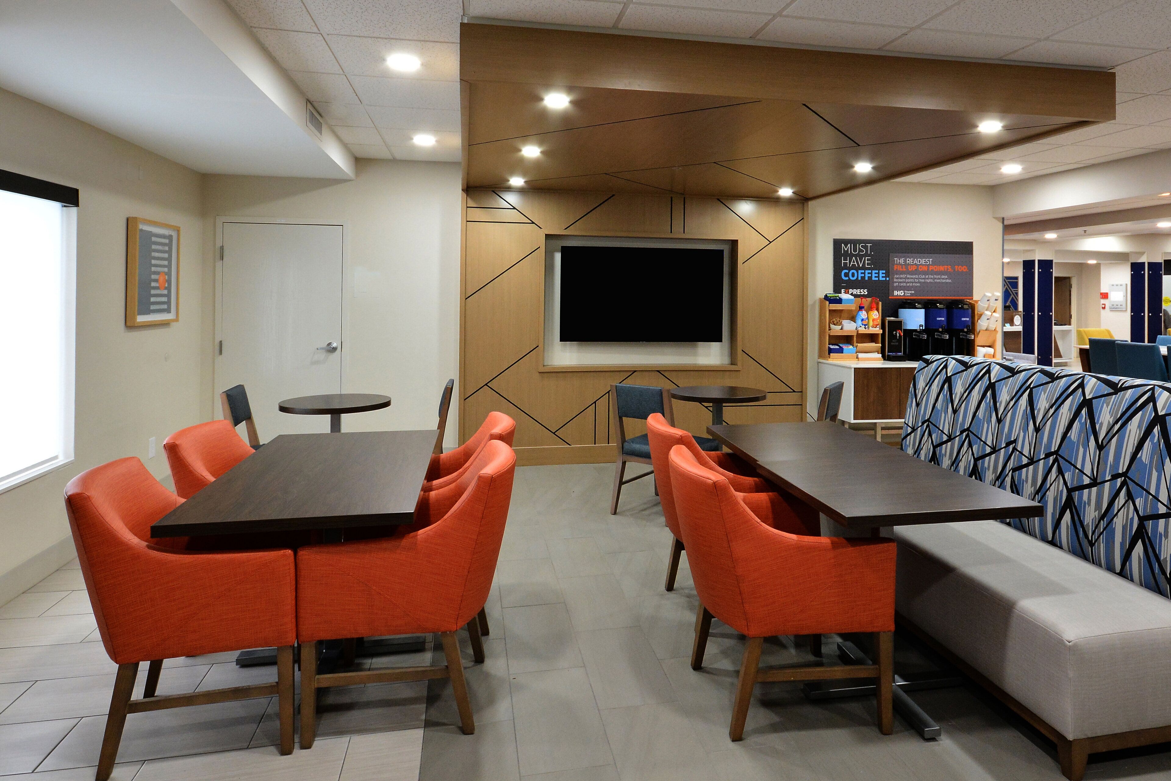 A modern meeting room with a large flat-screen TV, orange chairs, a long table, and a sofa.