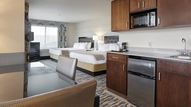 Habitación de hotel con comedor, kitchenette y cama con dos almohadas.