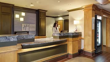 A hotel reception area with a marble counter, a digital display, and a refrigerator.