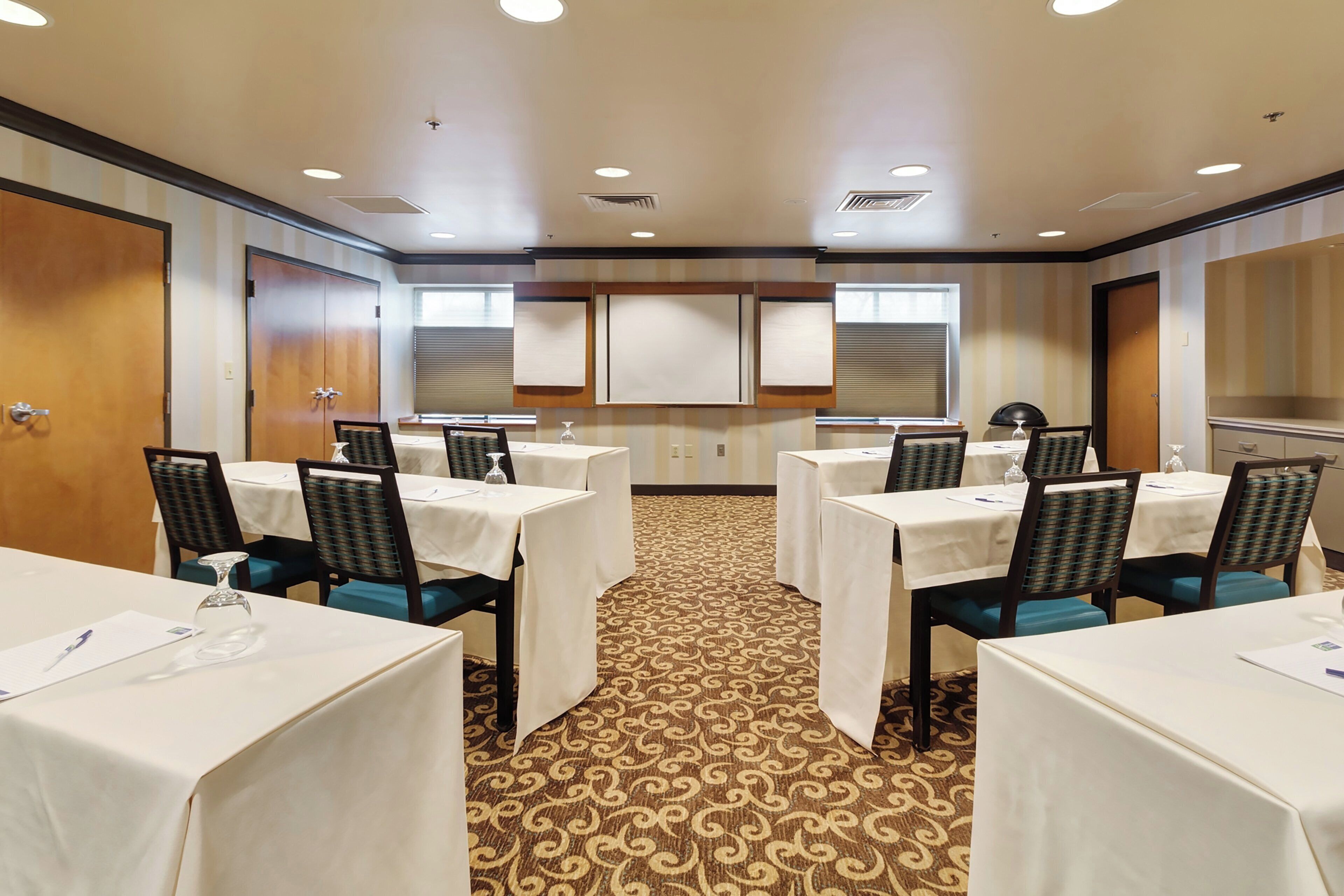 A conference room with multiple tables and chairs, a patterned carpet, and a neutral color scheme.