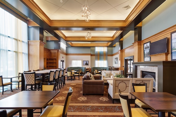 A spacious hotel lobby with a dining area, seating arrangements, and a fireplace.