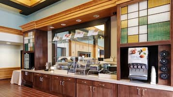 A self-service breakfast bar with a coffee machine, a refrigerated display case, and a juice dispenser.
