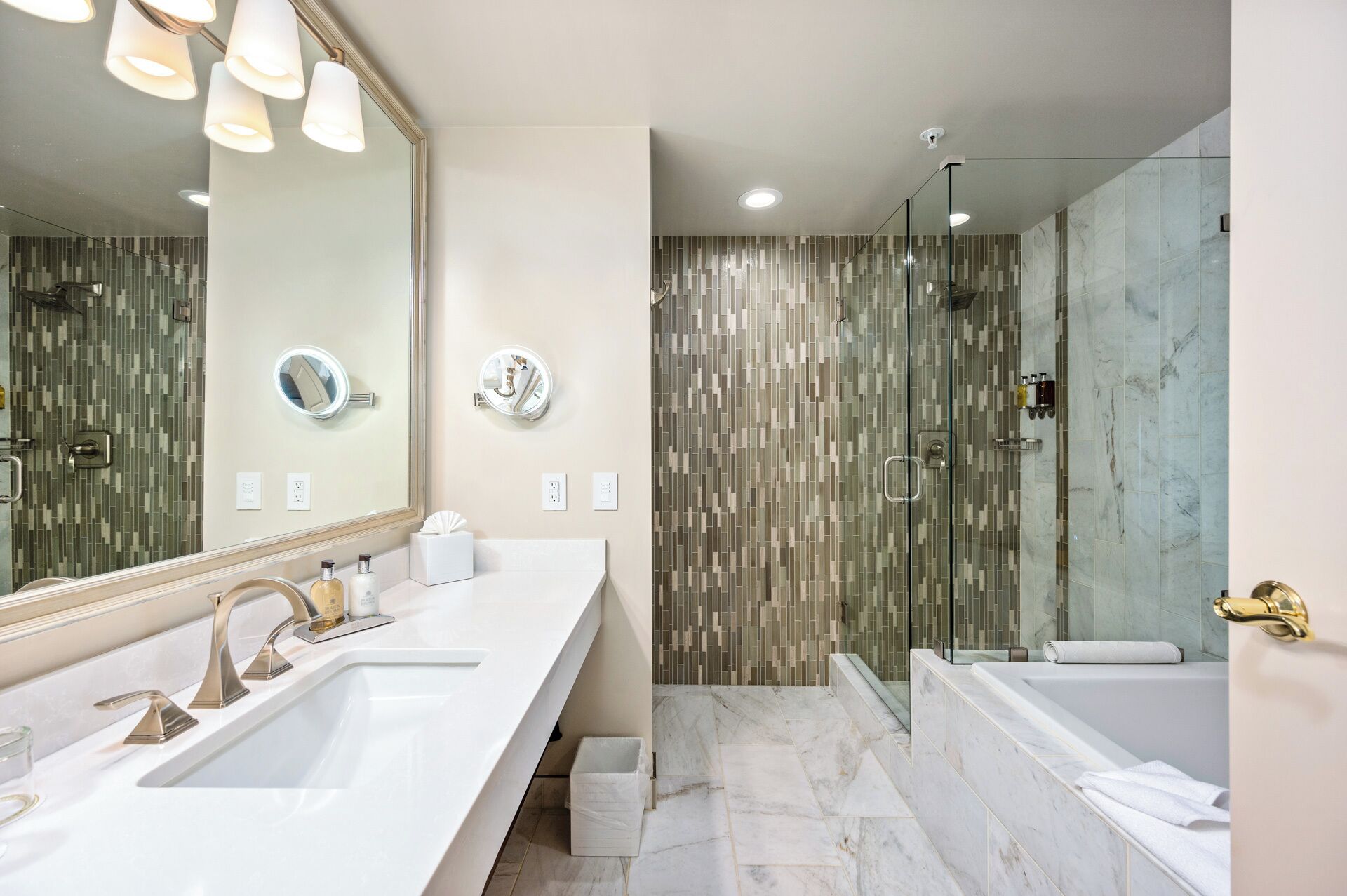 A modern bathroom with a large mirror, two sinks, a shower, and a bathtub.