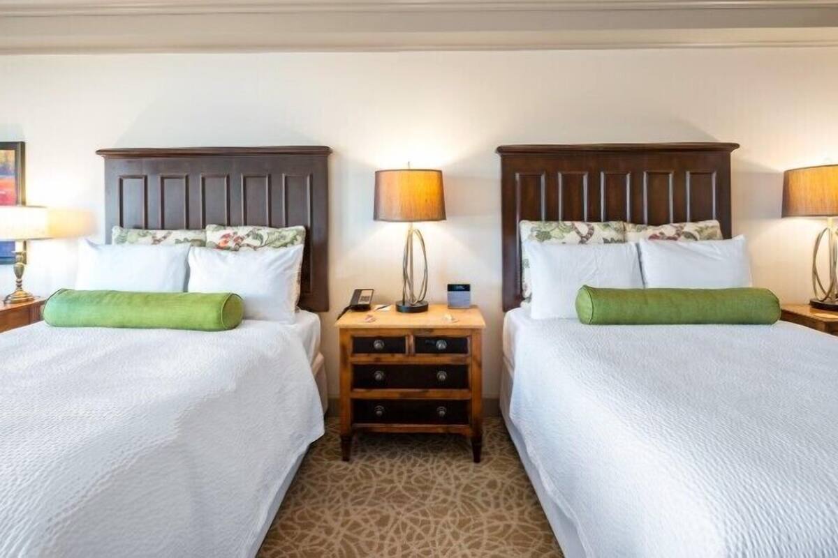 A hotel room with two beds, each with a wooden headboard, a nightstand, a lamp, and a painting on the wall.