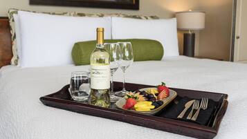 Una cama bien hecha con una bandeja que contiene una botella de vino, copas y una fuente de fruta.