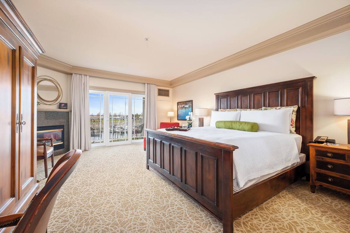 A spacious hotel room with a large bed, a wooden nightstand, a desk, and a view of the outdoors through a sliding glass door.