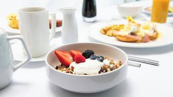 Uma mesa de café da manhã com um potinho de iogurte e granola, uma xícara de café e um prato com ovos e torradas.