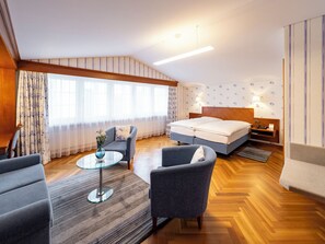 Une chambre d’hôtel moderne avec un grand lit, deux fauteuils, une table basse en verre et un plancher en bois.