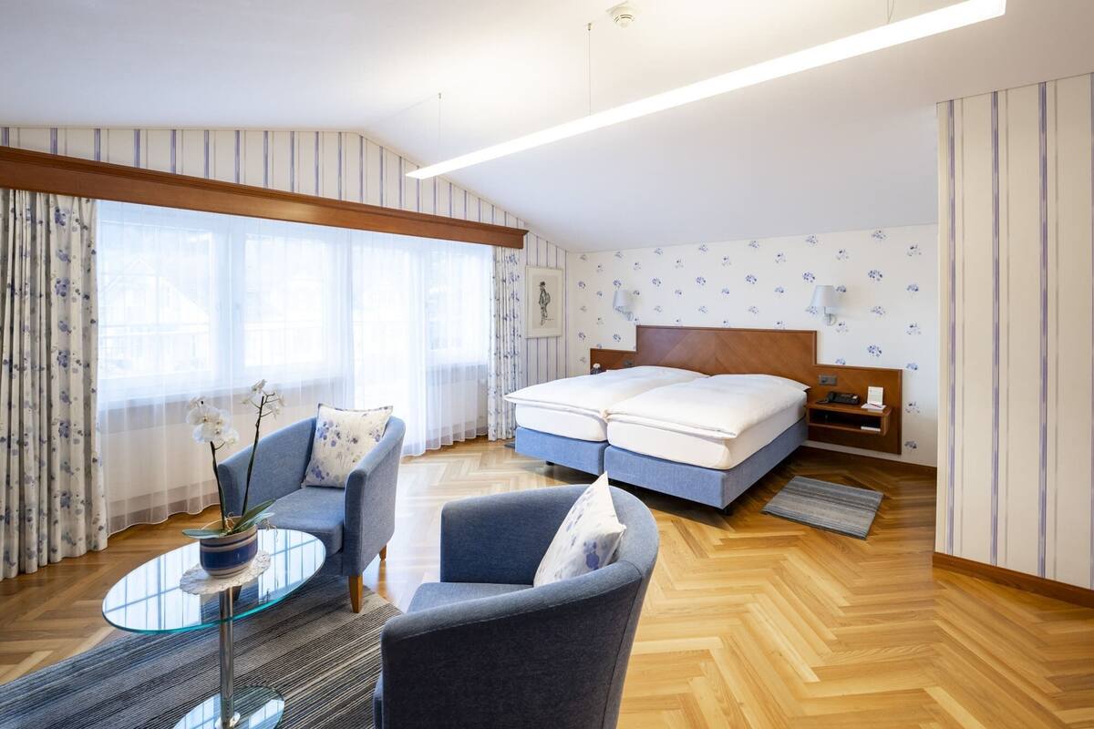 Habitació d'hotel amb un llit, un sofà, una taula petita i una finestra amb cortines.