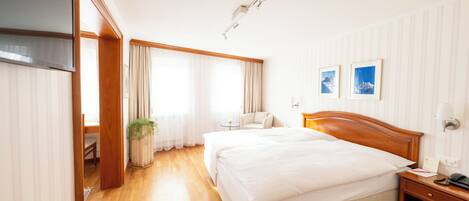 A hotel room with a large bed, a bedside table, a chair, a small table, and a potted plant.