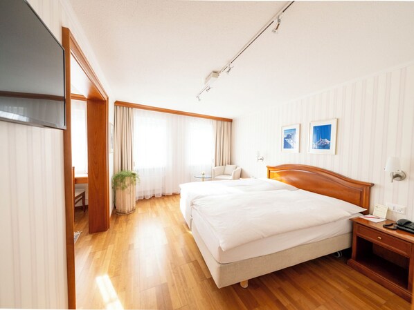 A hotel room with a large bed, a bedside table, a chair, a small table, and a potted plant.