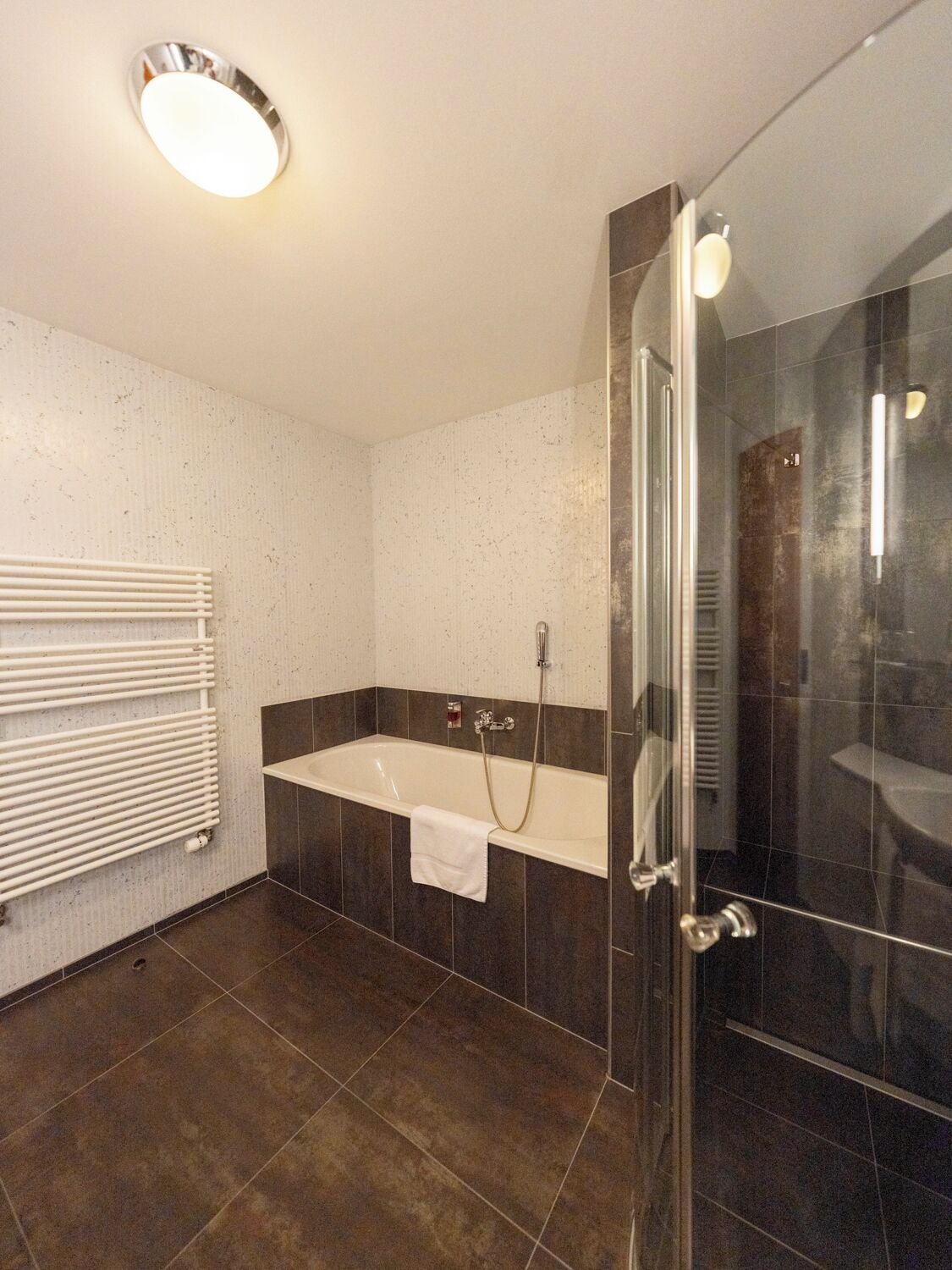 Un baño moderno con cabina de ducha de vidrio, una bañera blanca y un perchero para toallas.