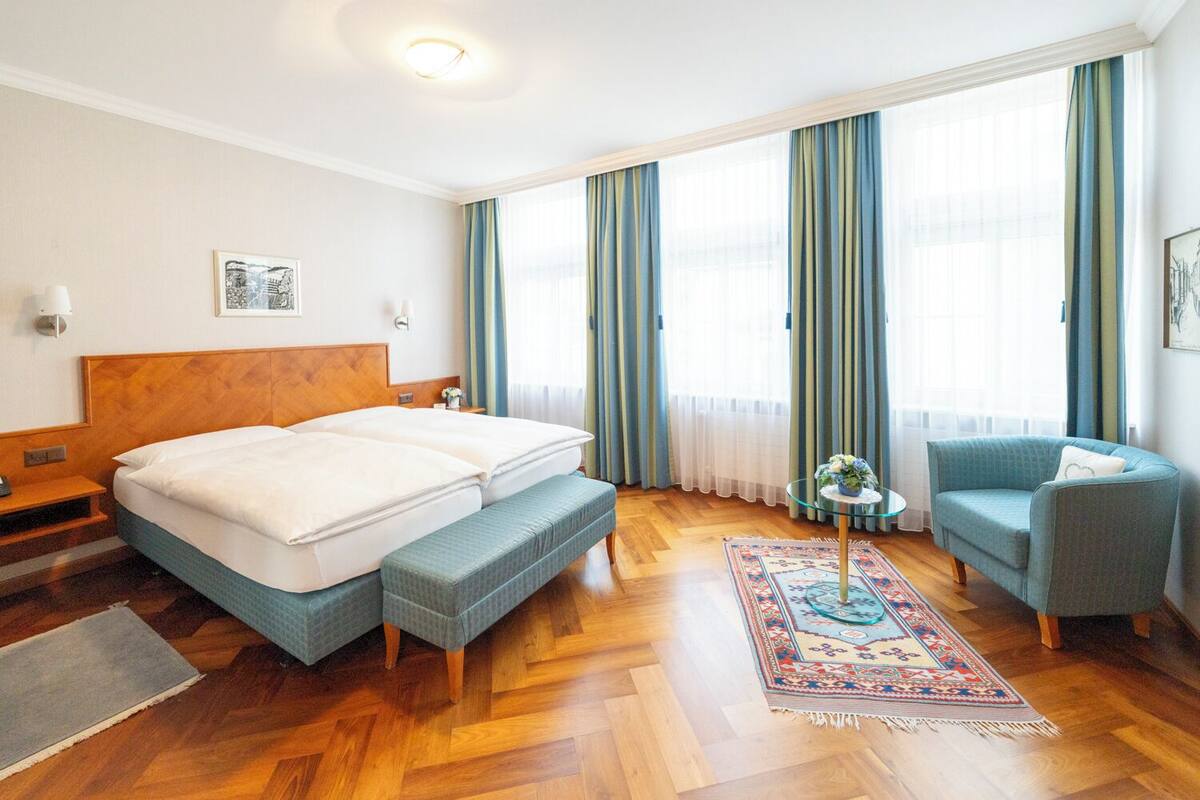 Habitació d'hotel amb llit doble, una panxa, una cadira, una taula petita i un feser decoratiu.