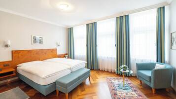 Habitación de hotel con cama doble, un banco, una silla, una mesita y un tapete decorativo.