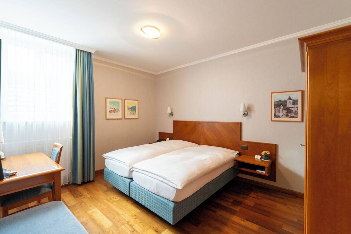 Habitació d'hotel amb un llit doble, un escriptori de fusta, una cadira, una taula petita amb un ram i un quadre a la paret.