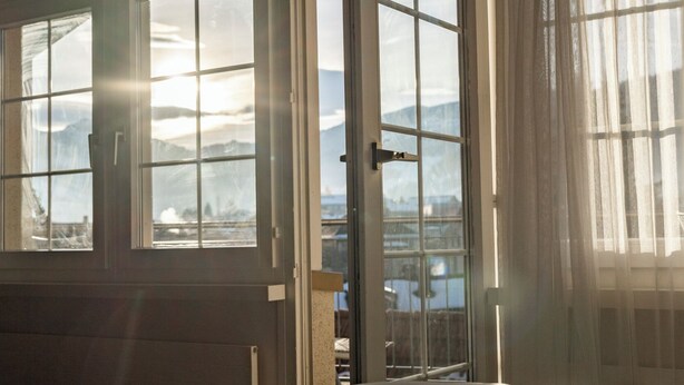 A bedroom with a large bed, a window with a view of mountains, and a door leading to a balcony.
