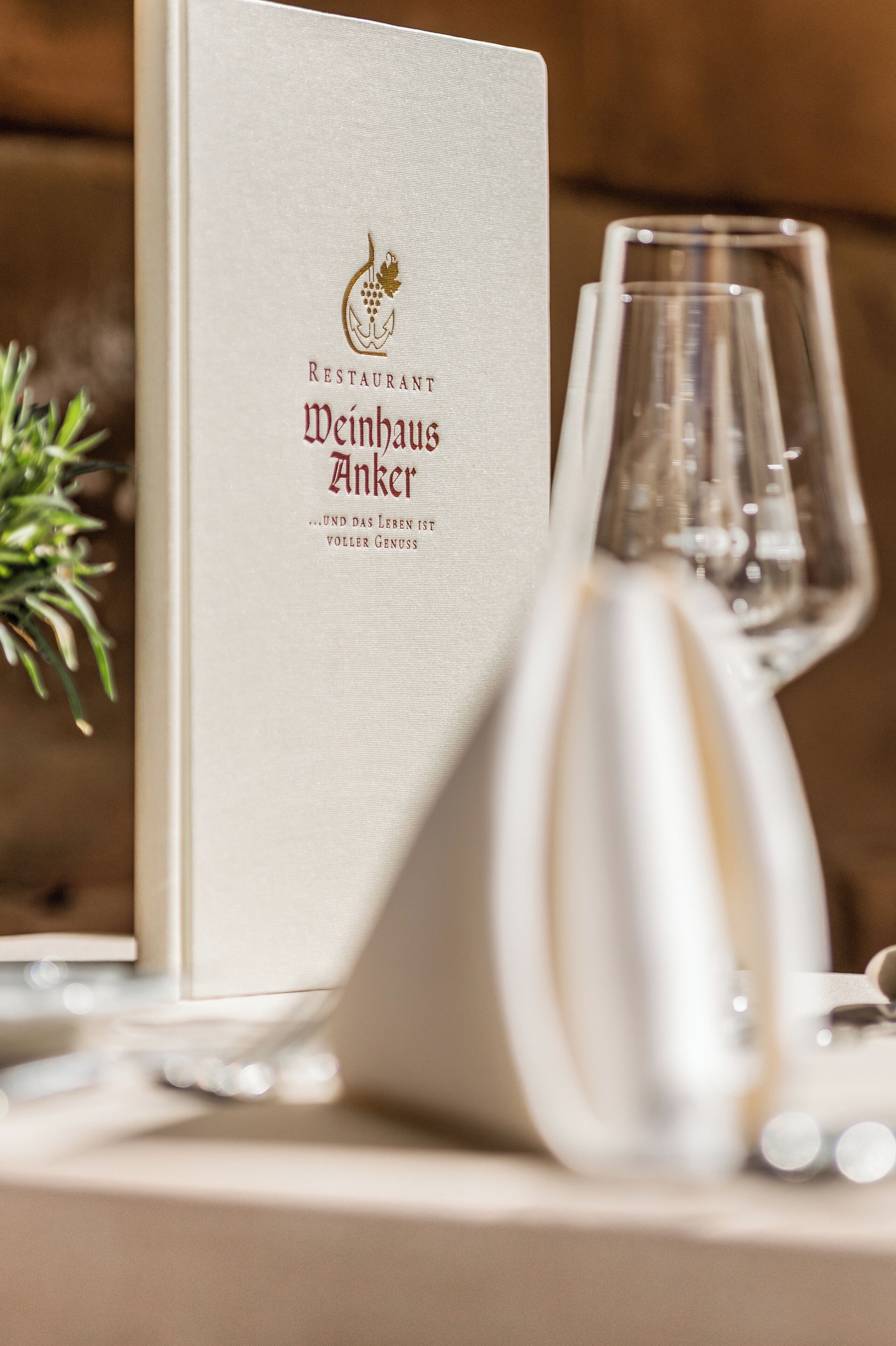 A menu titled "Restaurant Weinhaus Anker" with a wine glass and a decorative plant on the table.