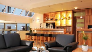 A modern living area with a bar, leather sofas, a wooden coffee table, and a potted plant. - Hotel Anker (Marktheidenfeld)
