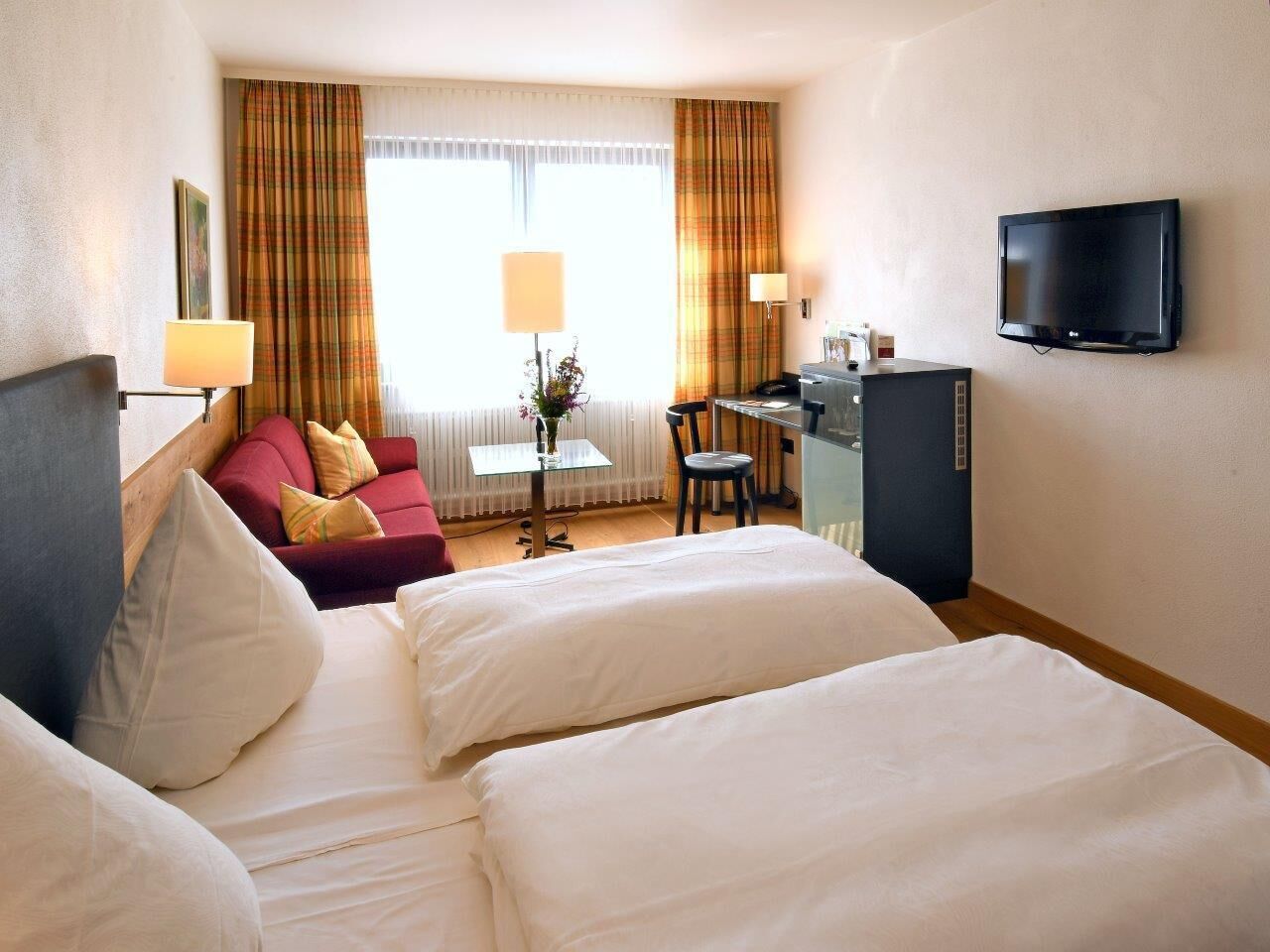 Habitación de hotel con dos camas, un escritorio, un televisor y un sofá.