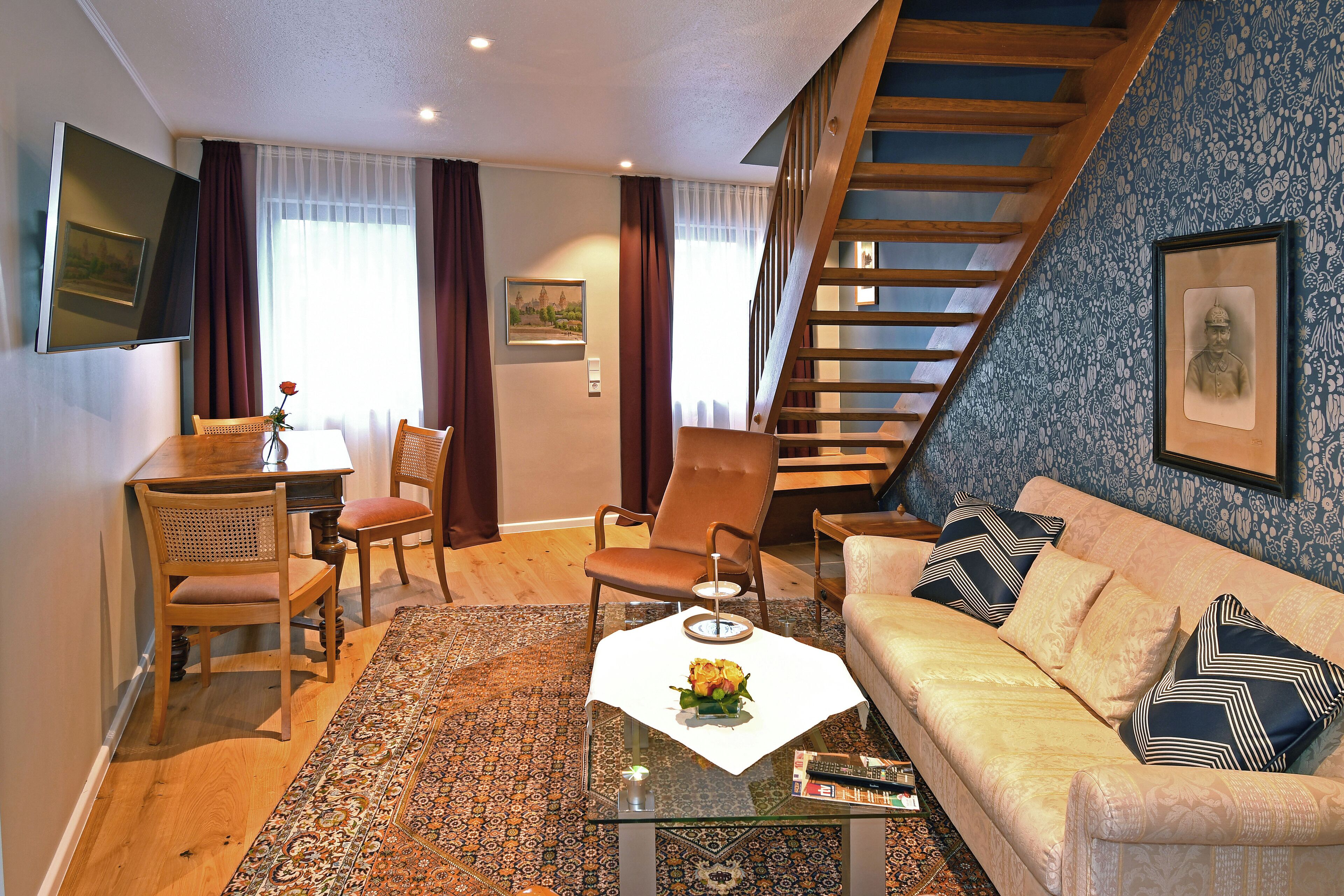 A living room with a sofa, chairs, a coffee table, a TV, and a staircase.