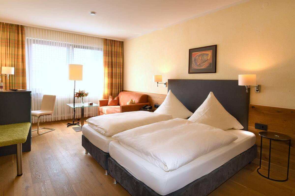Quarto de hotel com duas camas, uma escrivaninha, uma cadeira, um sofá e uma televisão.