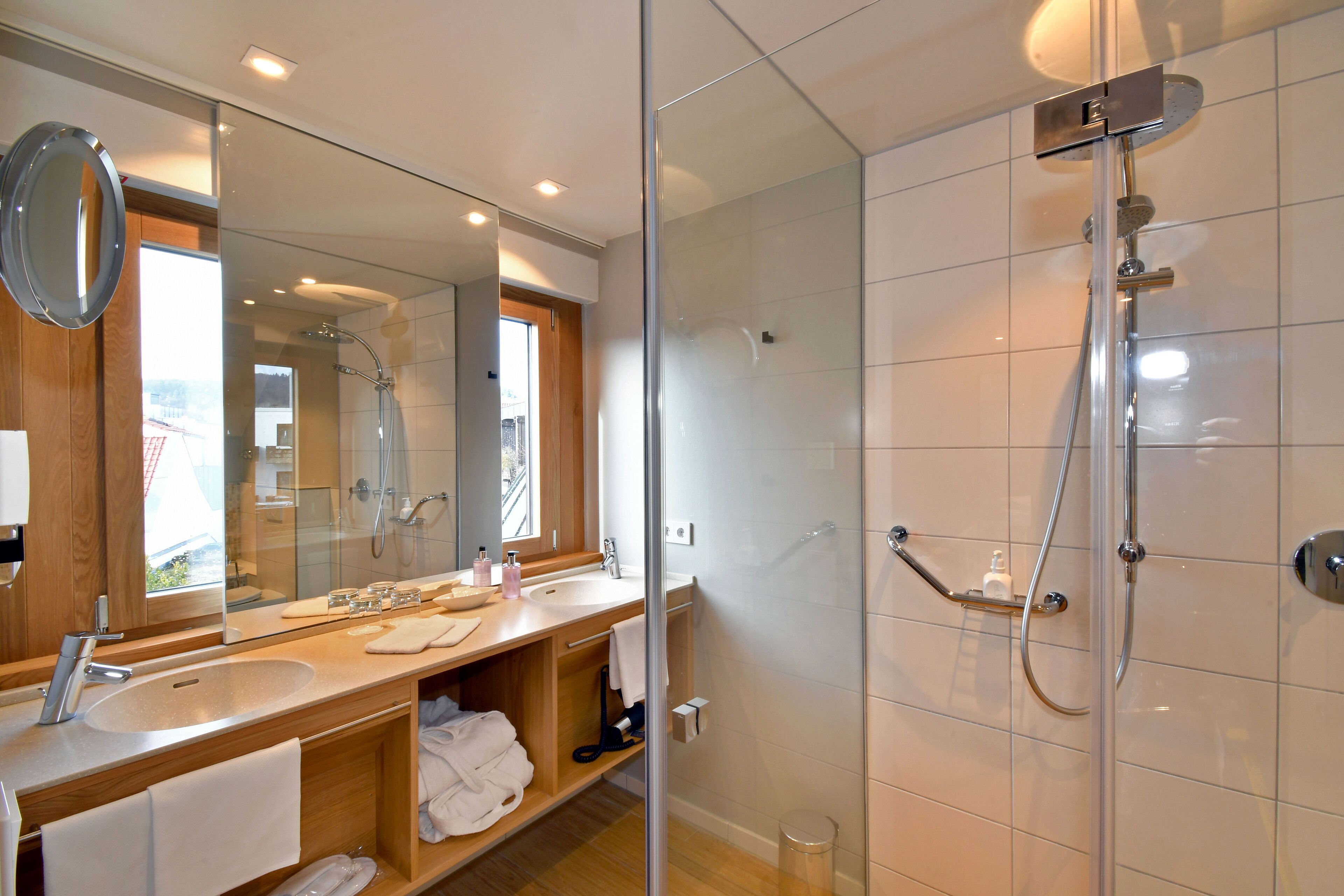 A modern bathroom with a glass-enclosed shower, a large mirror, and a wooden vanity with a sink and towel rack.
