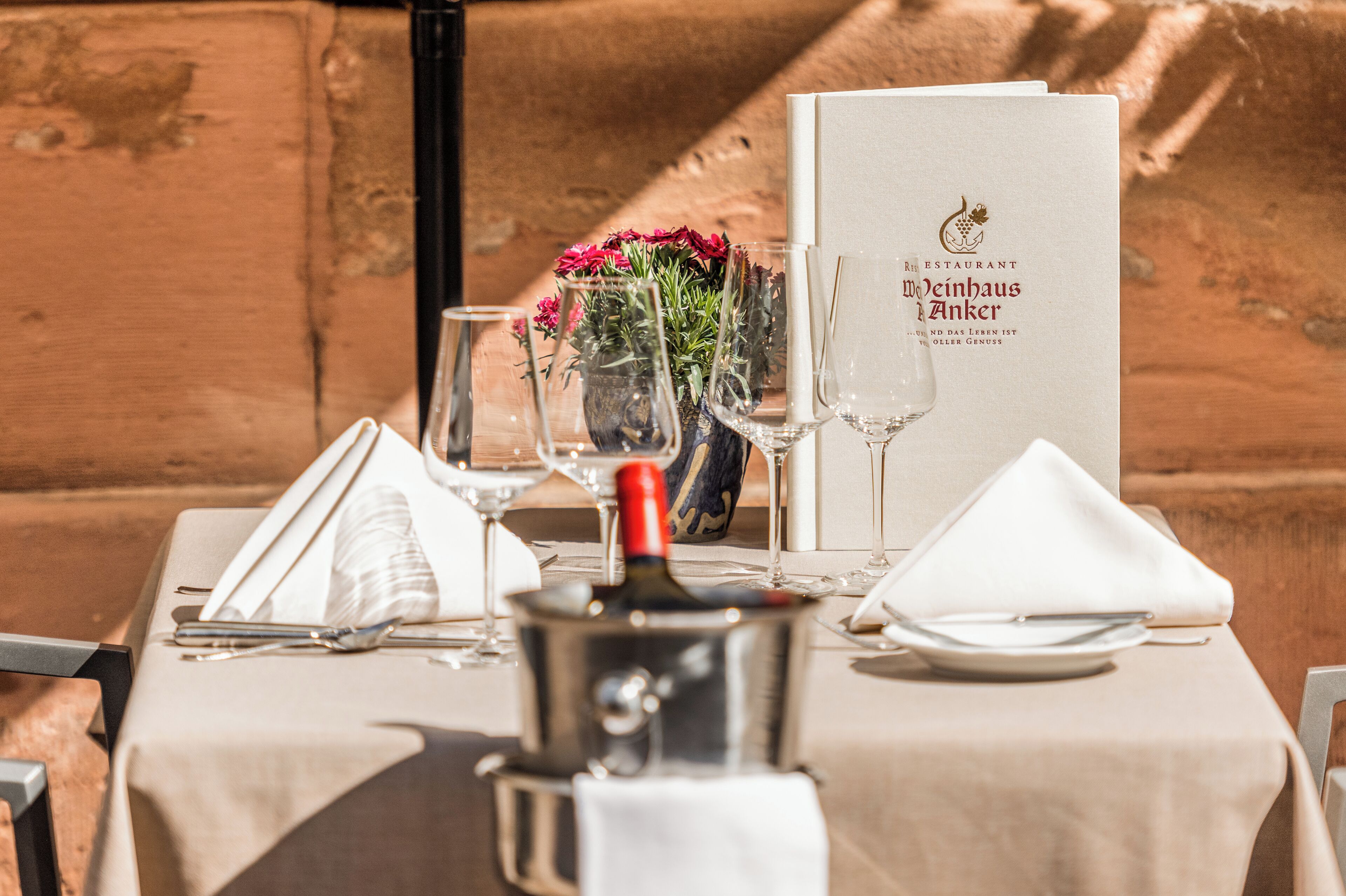 A table set for dining with a menu, wine glasses, a bottle of wine, and a vase of flowers.