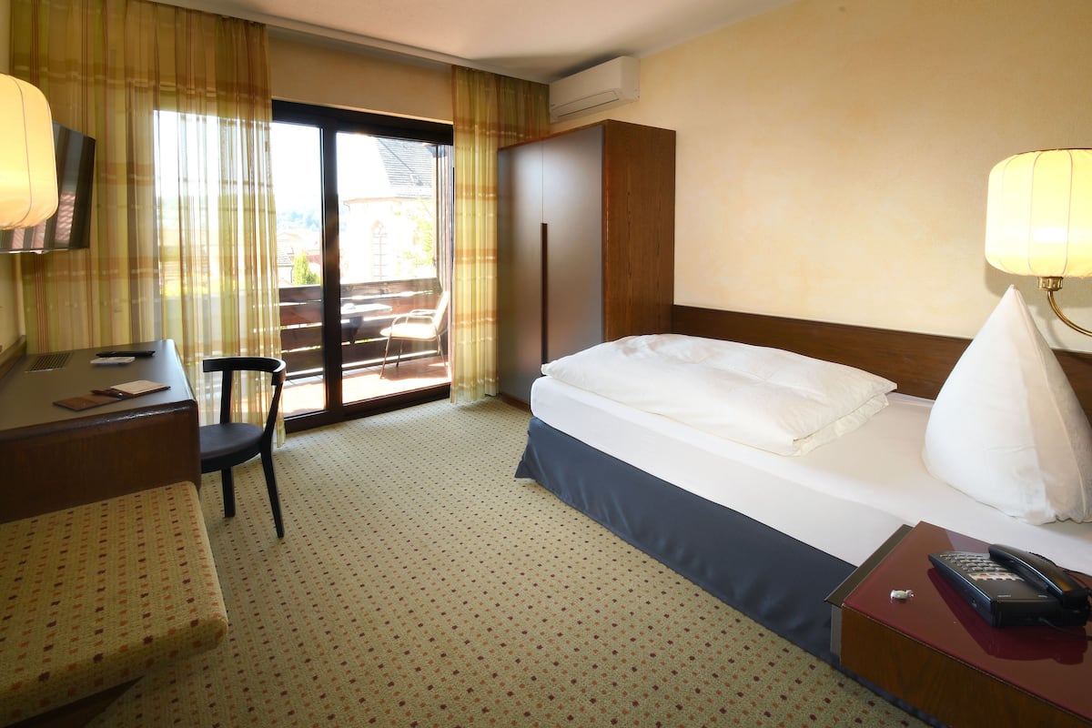 Quarto de hotel com cama, escrivaninha, cadeira e vista pela janela.