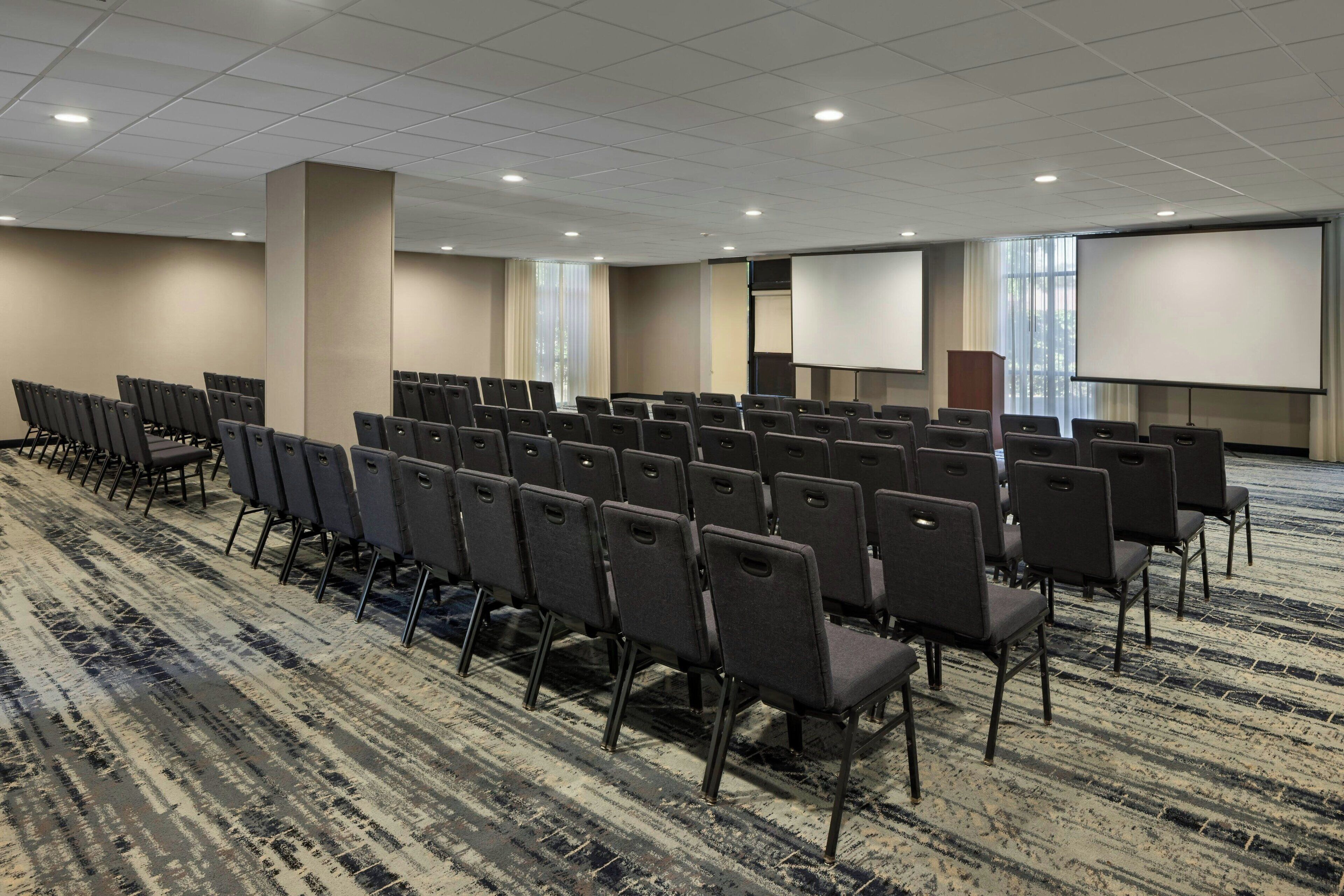 A conference room with rows of chairs, a carpeted floor, and a projector screen.