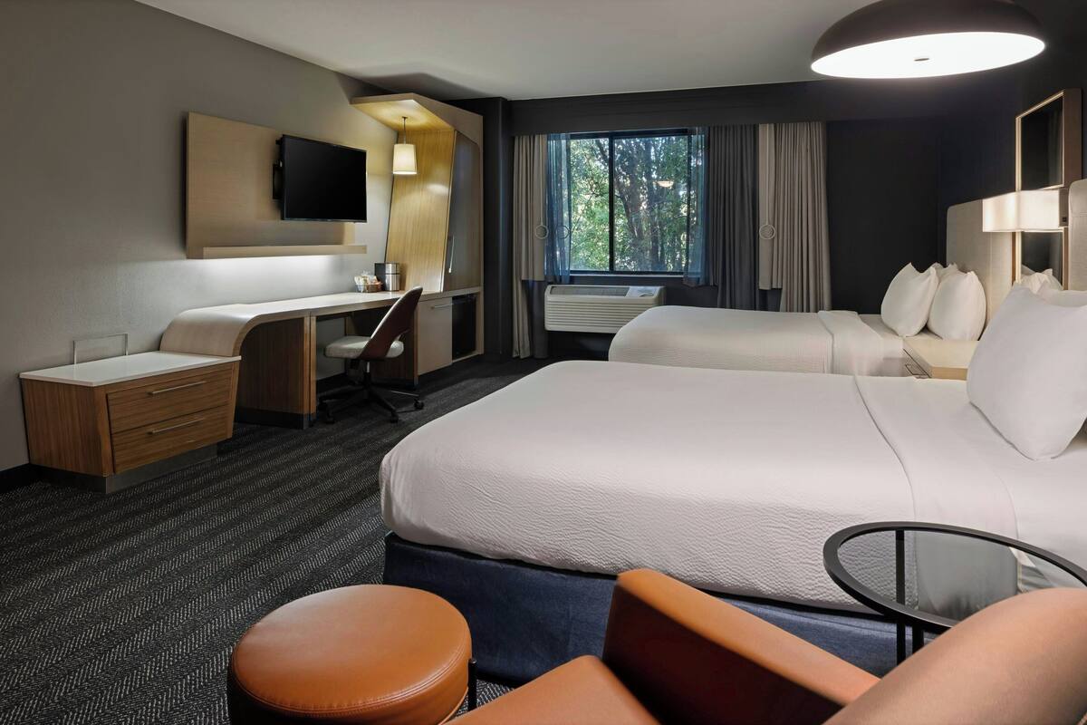 A hotel room with a large bed, a desk, a chair, a small table, and a TV mounted on the wall.