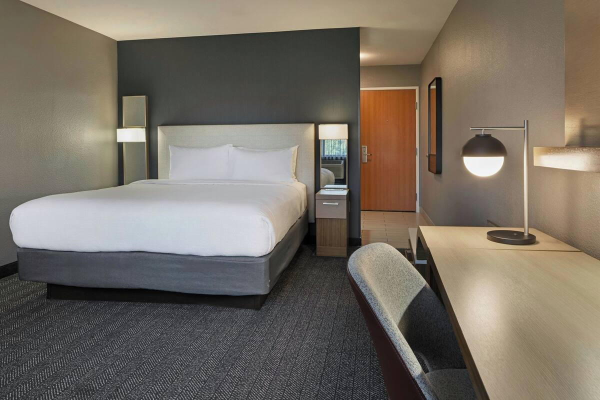 A hotel room with a large bed, bedside tables, a desk, and a chair.