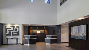 A modern reception area with a reception desk, a large abstract painting, and a view of the sky through small windows.
