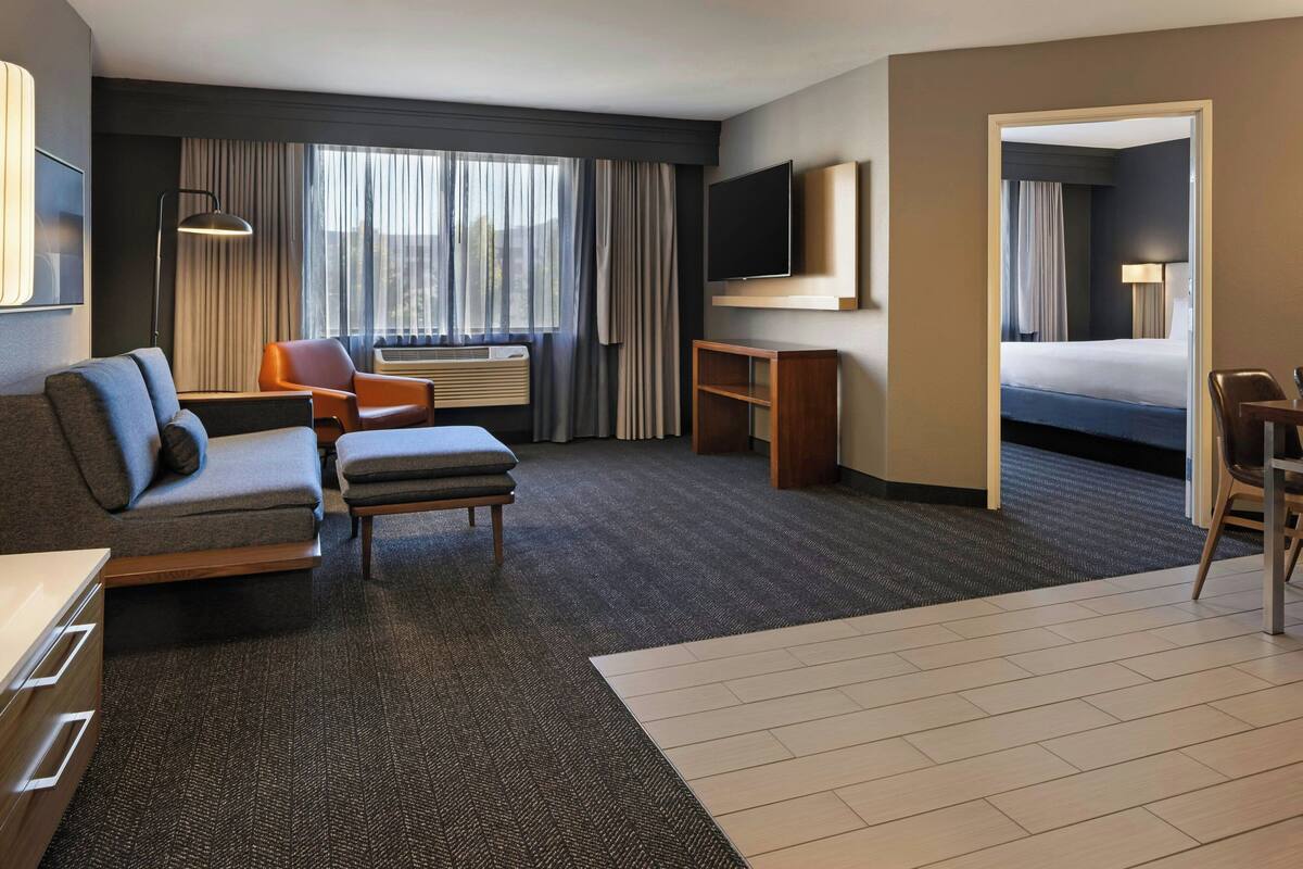 A hotel room with a sofa, armchair, desk, and a bed.