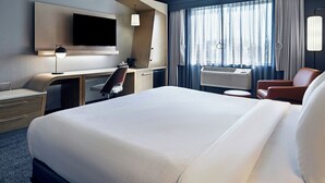 A modern hotel room with a large bed, a desk, a chair, a TV, and a window with curtains.