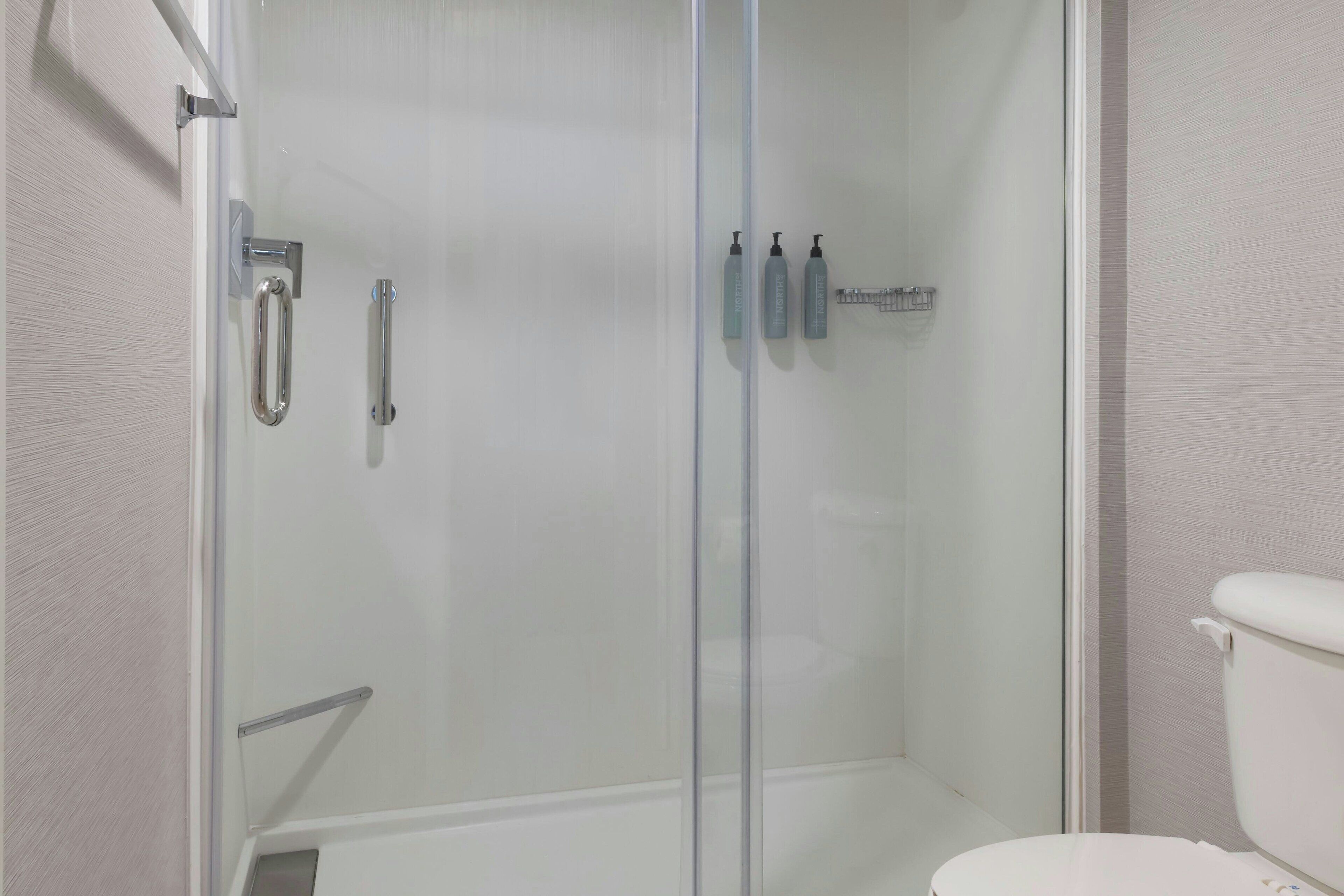 Un baño con ducha de vidrio, inodoro y repisa con artículos de aseo.