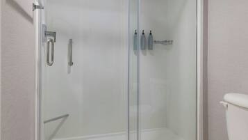Un baño con ducha de vidrio, inodoro y repisa con artículos de aseo.