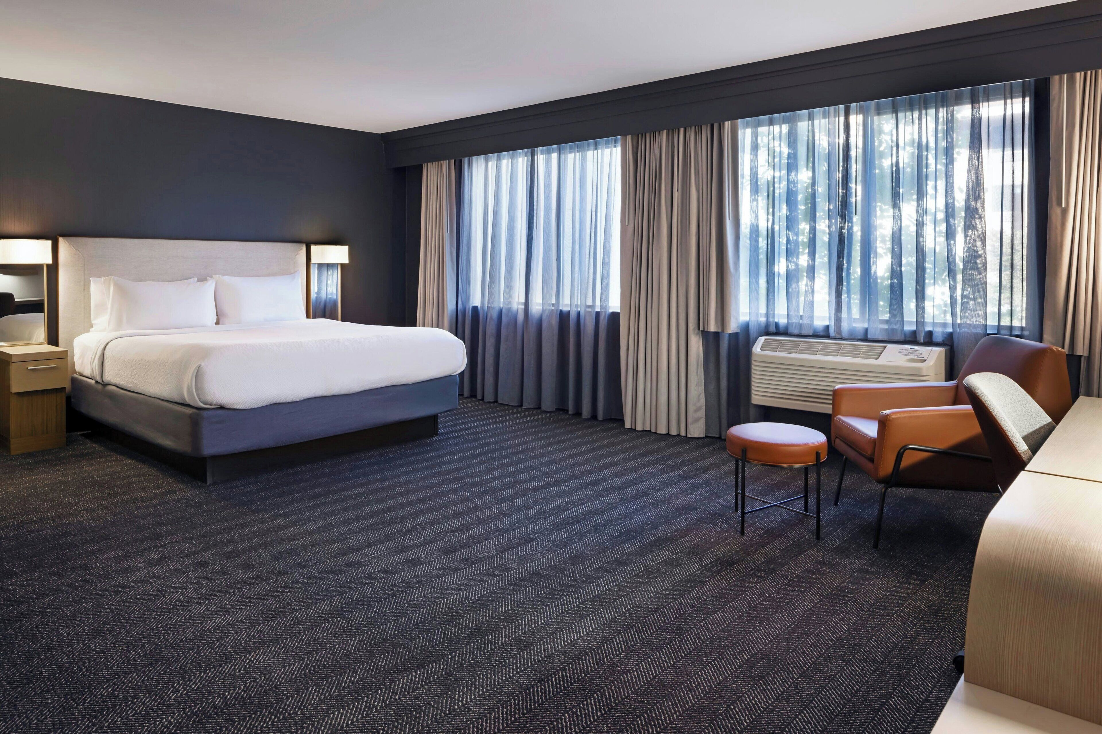 A hotel room with a large bed, a desk, a chair, and a window with curtains.