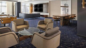 A modern hotel lobby with a seating area, a bar, and a large TV screen.