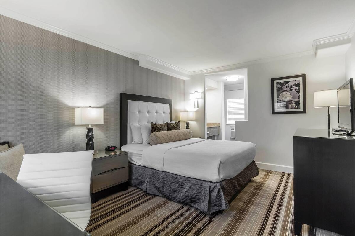 Une chambre d’hôtel avec un grand lit, un bureau, une chaise, une commode et un miroir.
