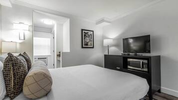 A hotel room with a large bed, a flat-screen TV, a microwave, and a desk with a lamp.